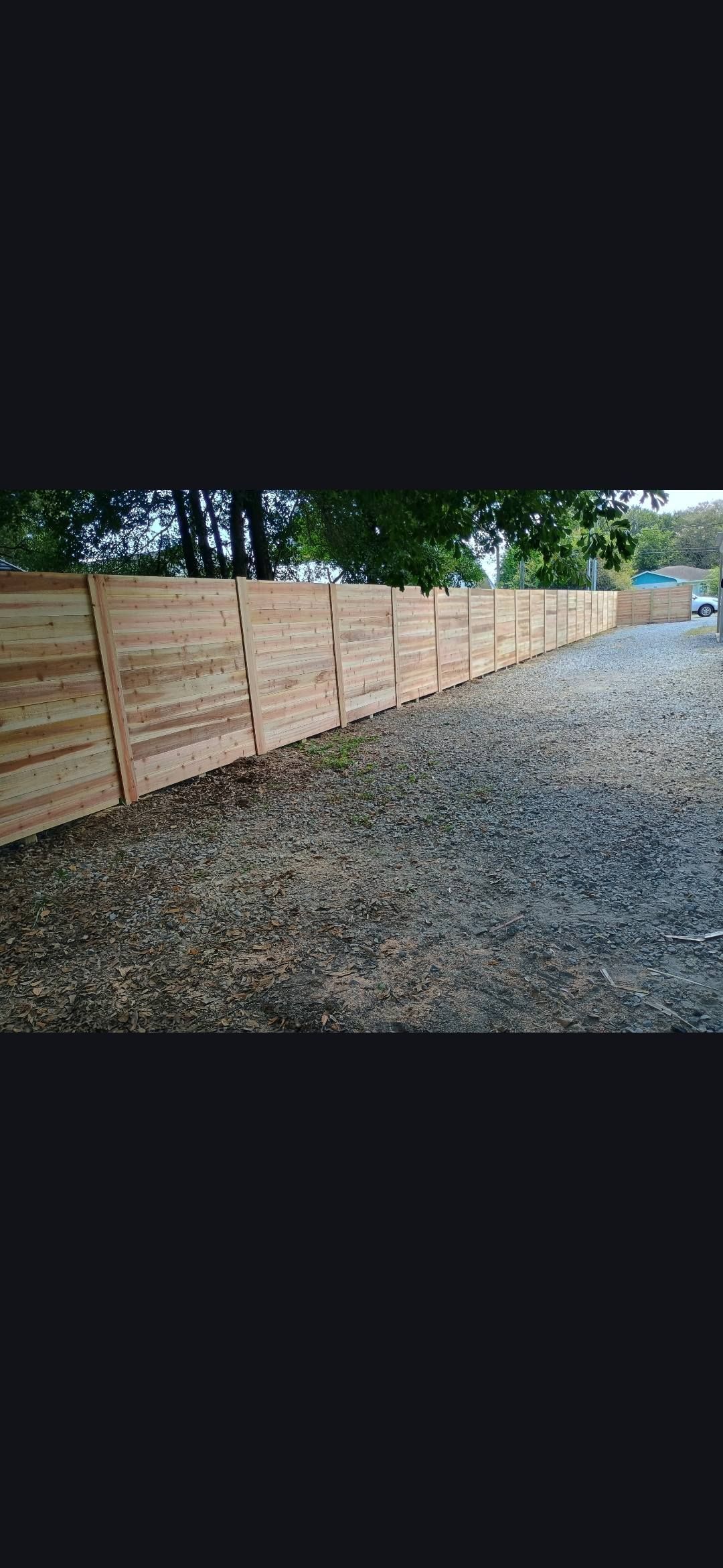 Gravel path beside a wooden fence under trees, with a narrow road in the distance