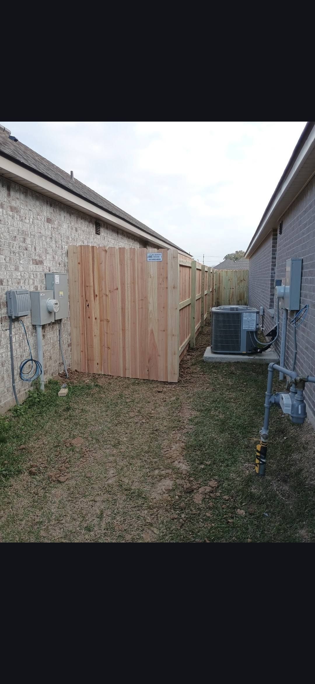 Narrow backyard between two buildings with a wooden fence and an air conditioner unit.