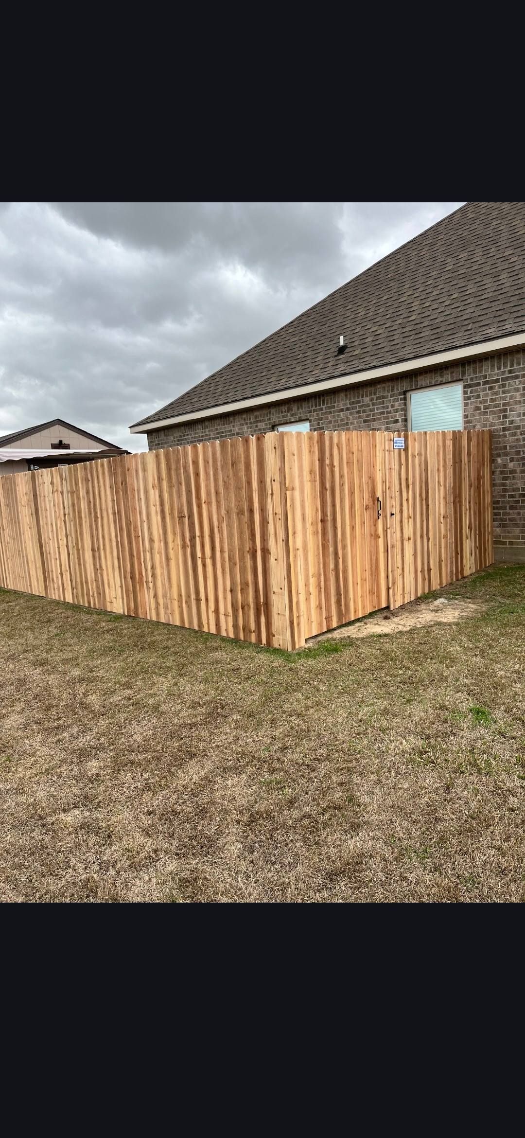 Wooden privacy fence beside a house under a cloudy sky