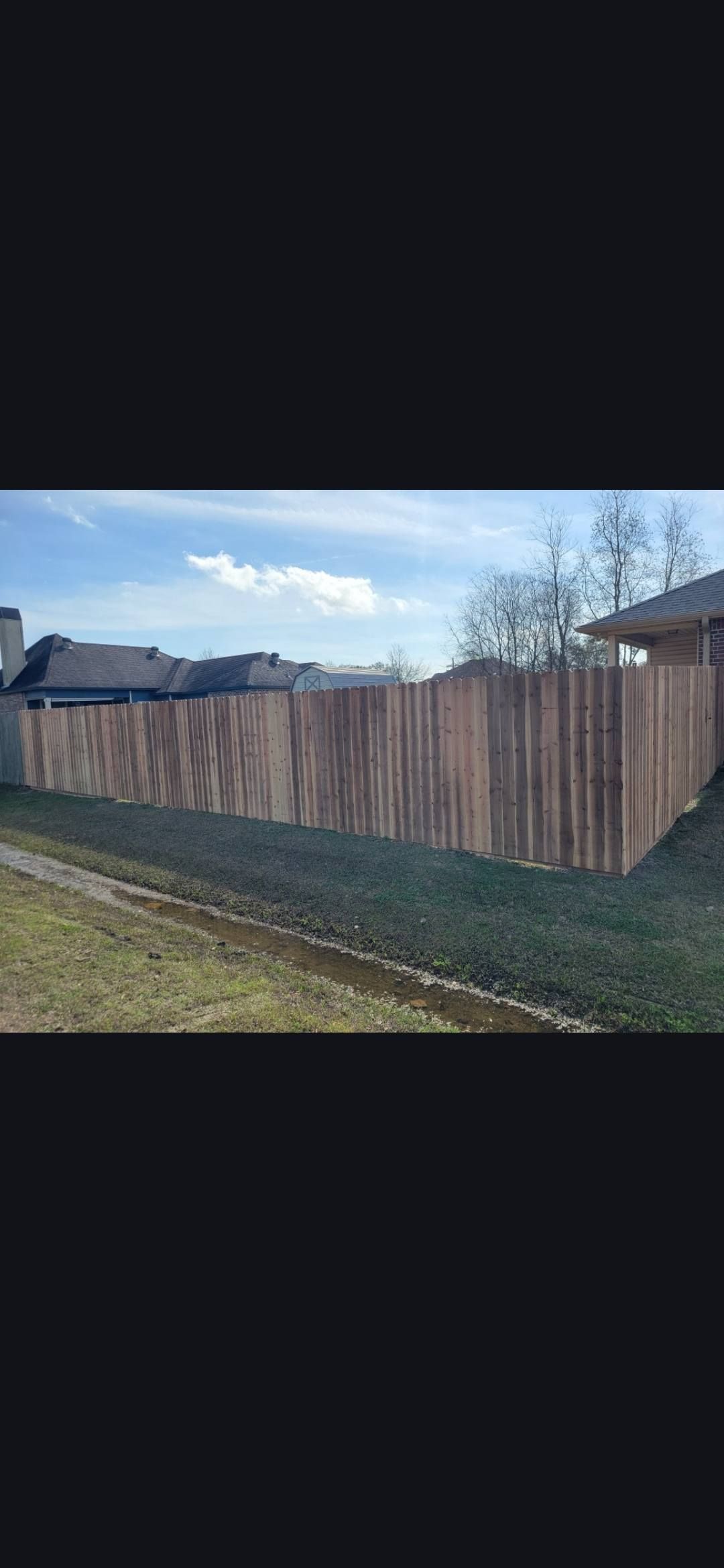 Long wooden privacy fence beside a grassy yard under a blue sky