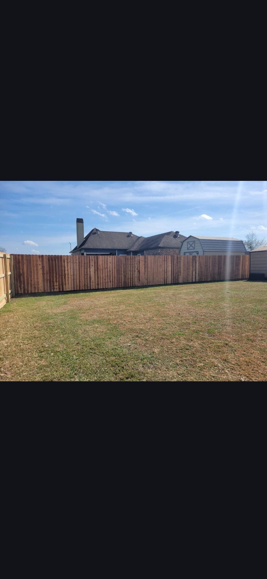 Backyard with a wooden fence, grassy lawn, and houses under a clear blue sky
