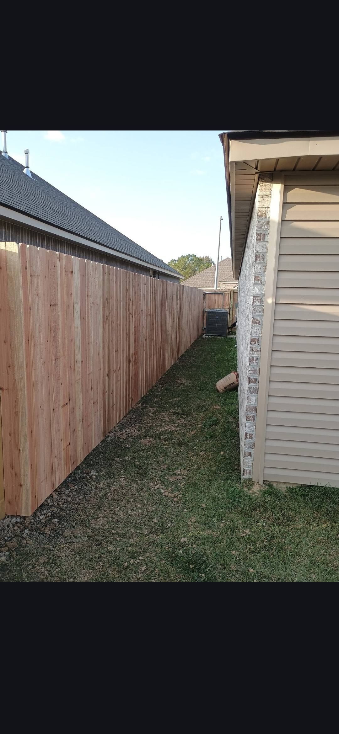 Narrow grassy alley between a wooden fence and a beige house in daylight