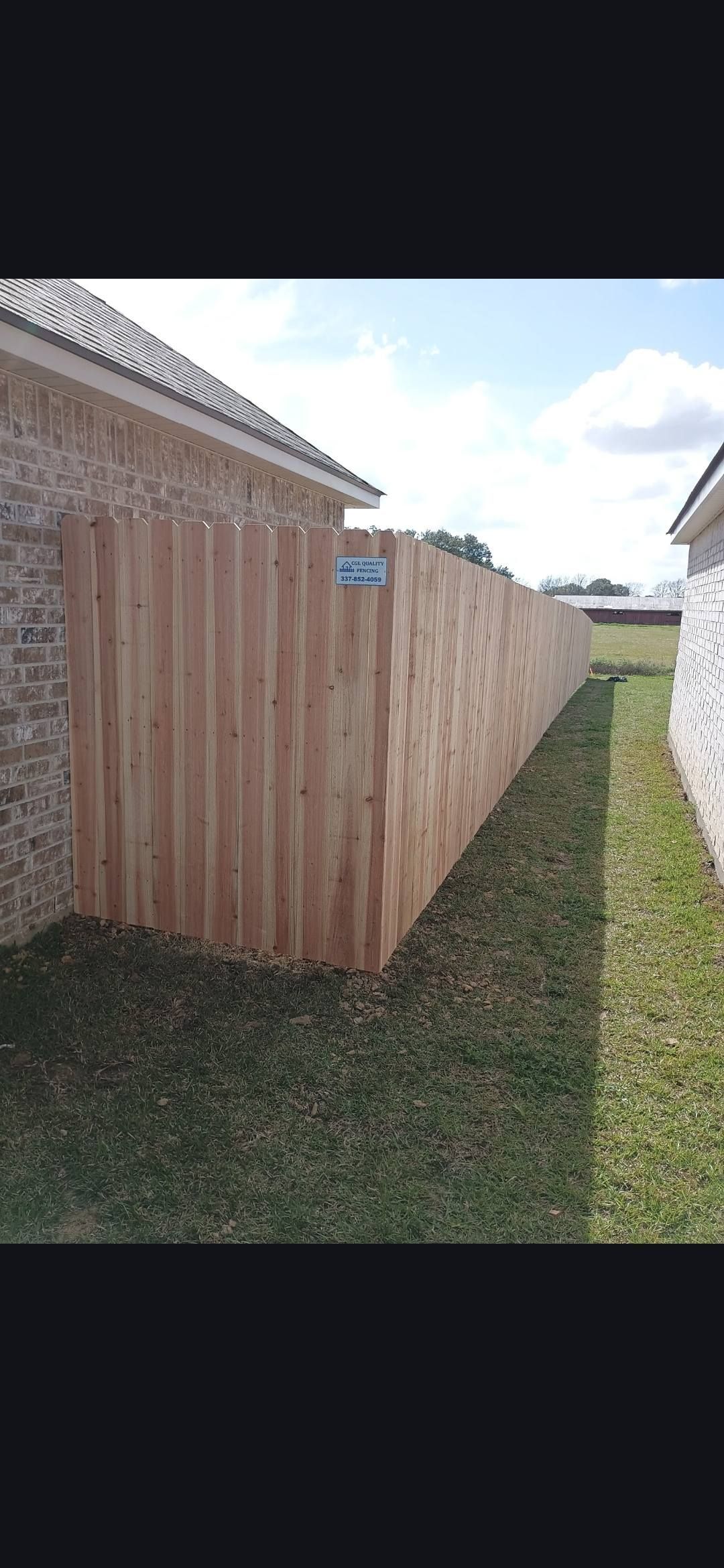 Wooden privacy fence beside a grassy yard, with houses on either side and a narrow pathway alongside it.