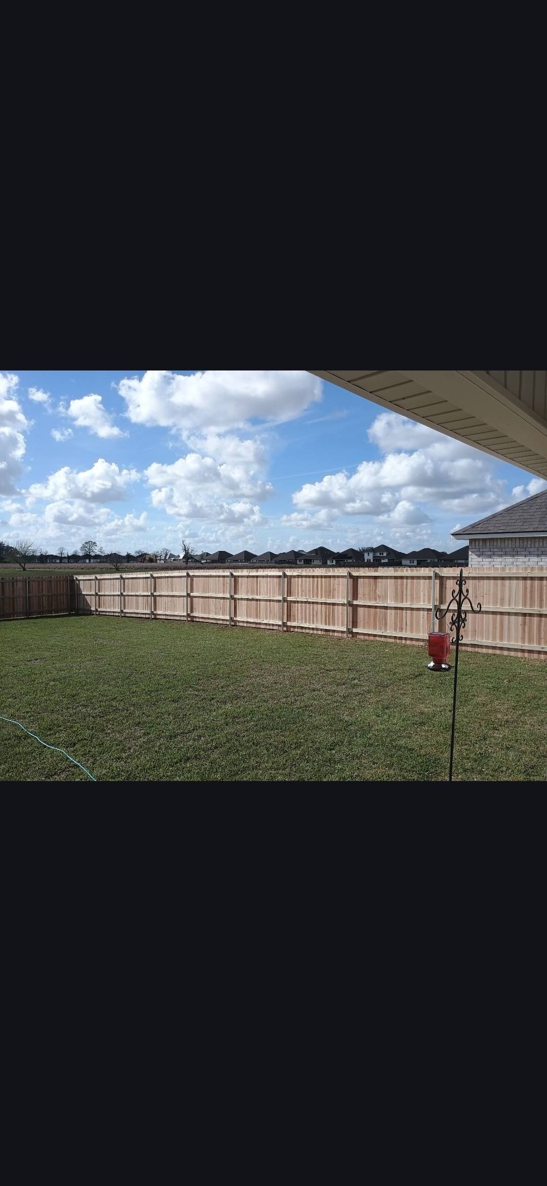 Wide grassy field under cloudy sky beside a long beige fence and building overhang