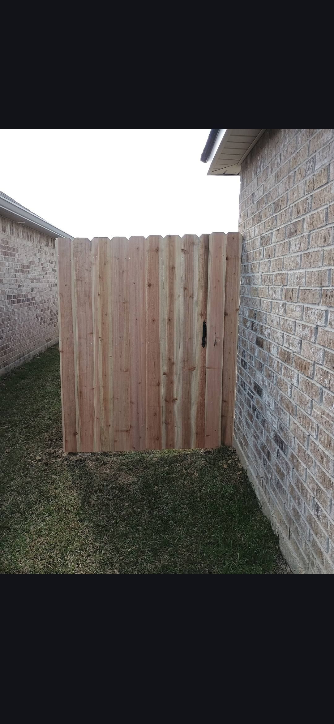 Wooden privacy gate between two brick walls in a narrow grassy side yard
