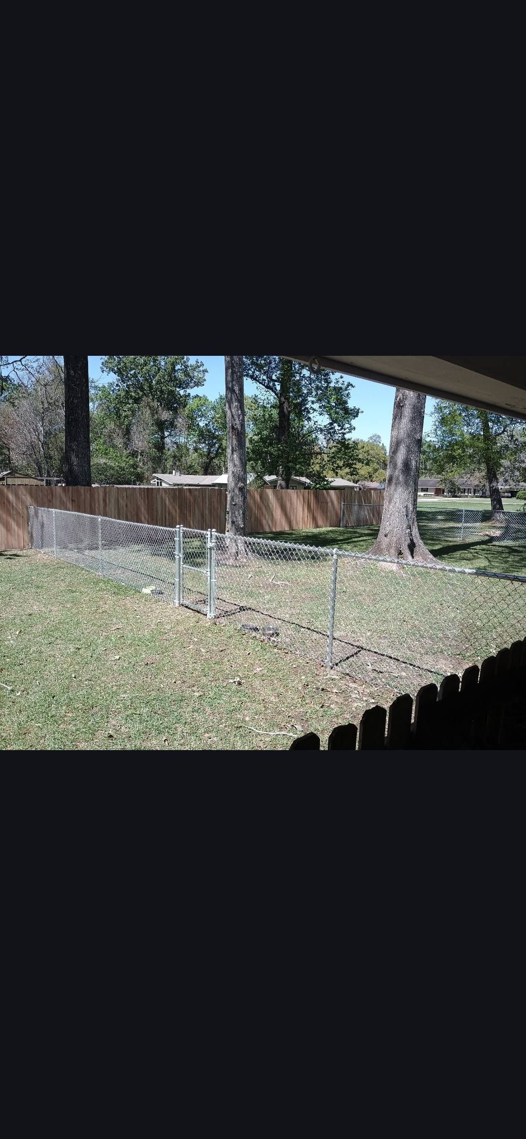 Shaded backyard with a stone bed, brown fence, trees, and hanging white icicles or streamers from a roof edge