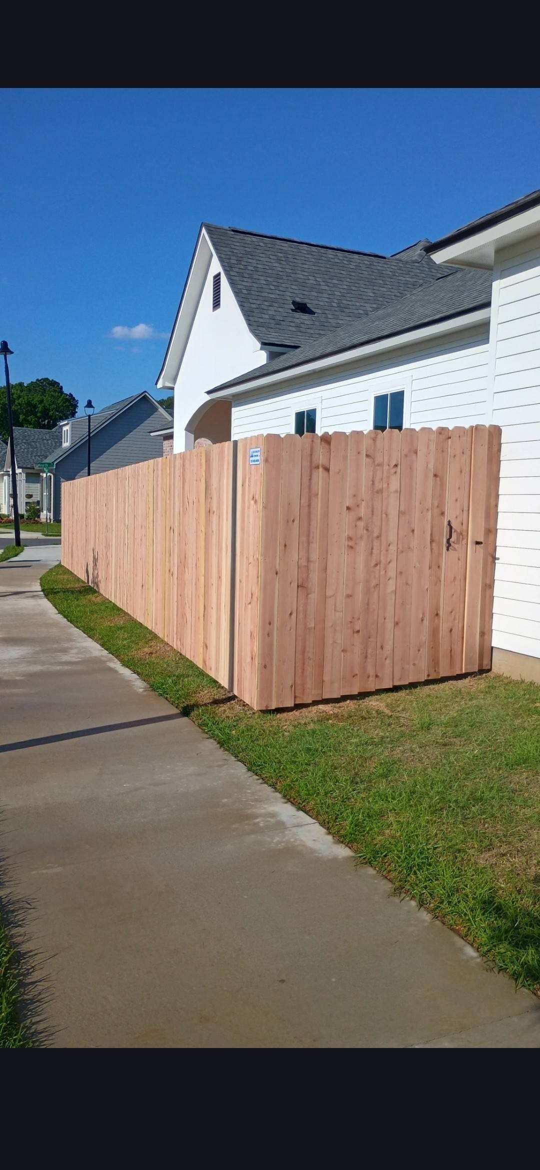 Wooden privacy fence beside a wet sidewalk next to a white house under a clear blue sky