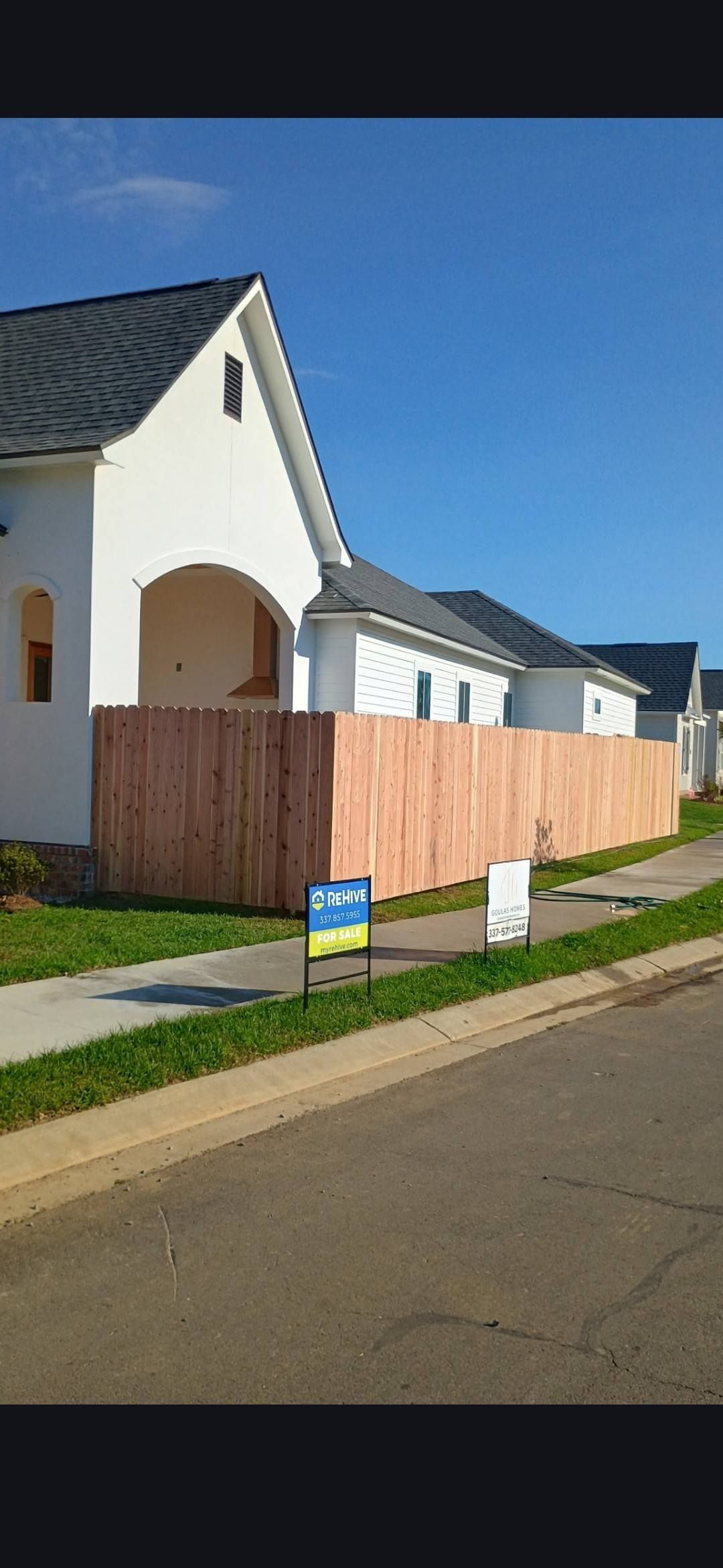 Suburban house with white walls, brown fence, and blue sky along a quiet street