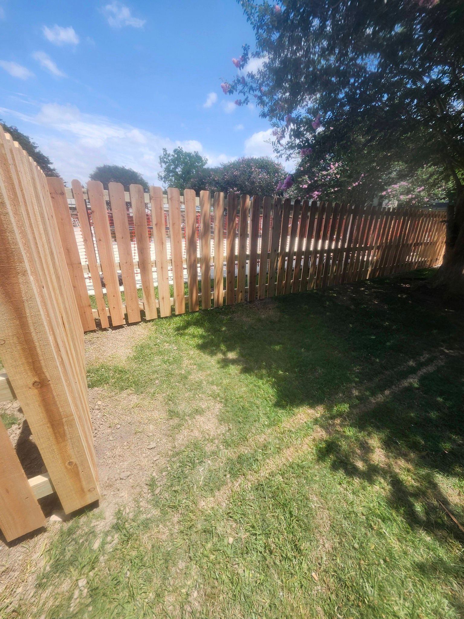 Wooden picket fence along a grassy yard in bright sunlight, with trees casting shade.