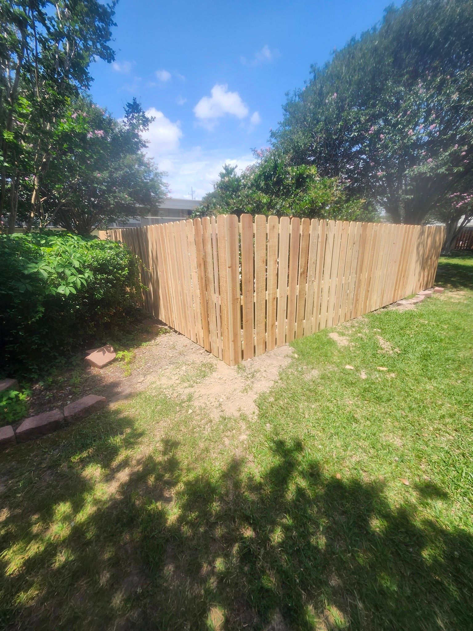 Wooden fence corner in a sunny backyard with green grass and trees under a blue sky
