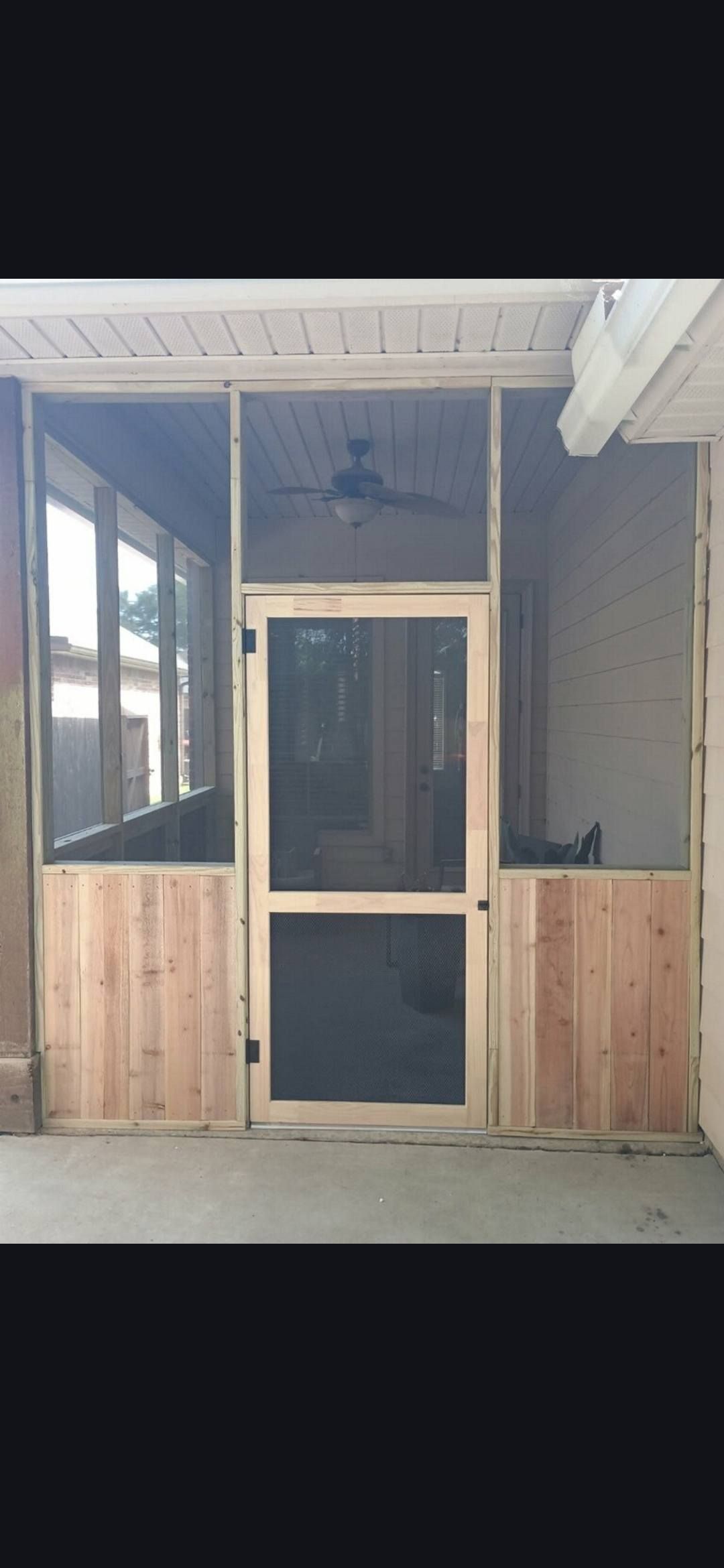 Covered porch with a screened door, wood paneling, and side windows under a roof.