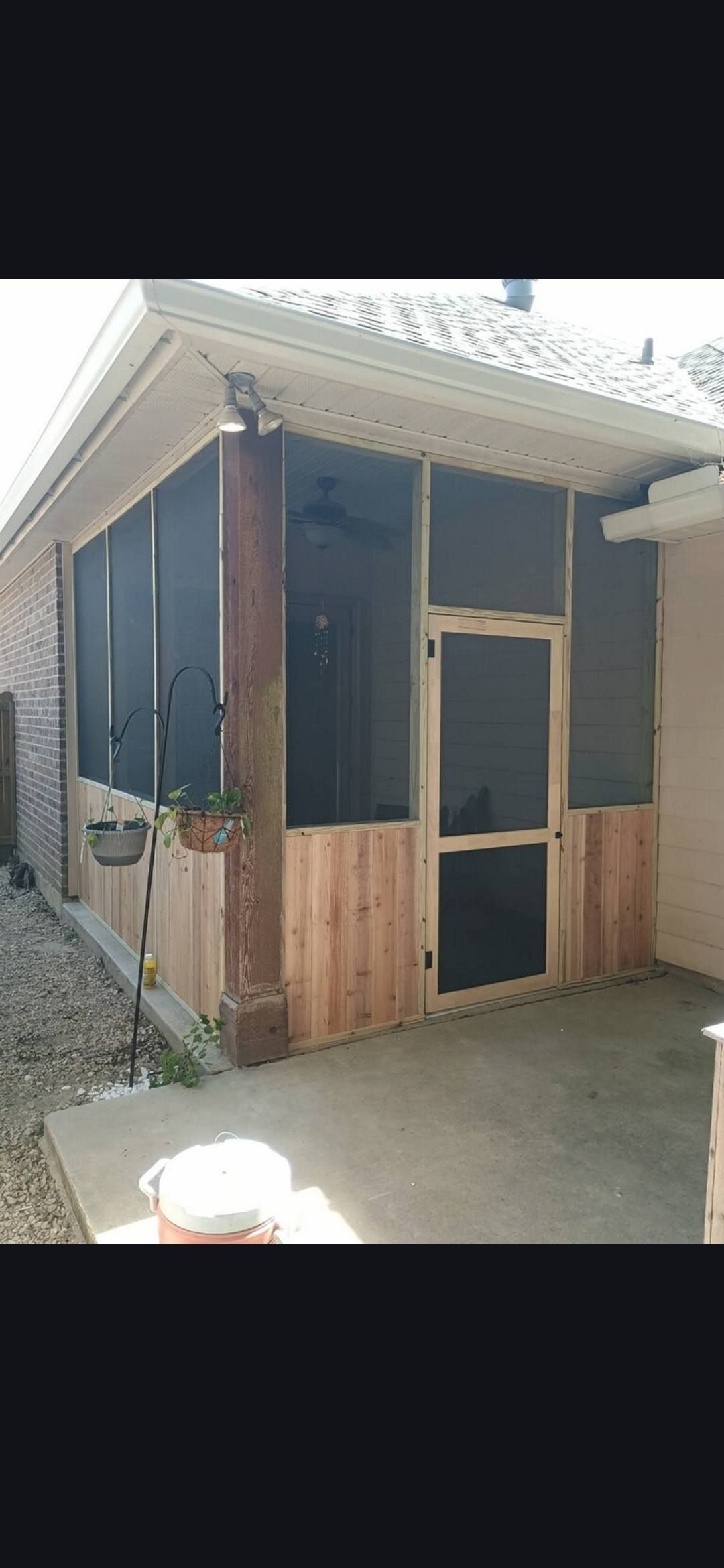 Small wooden porch entrance on a brick house with dark shutters and a screen door in front.