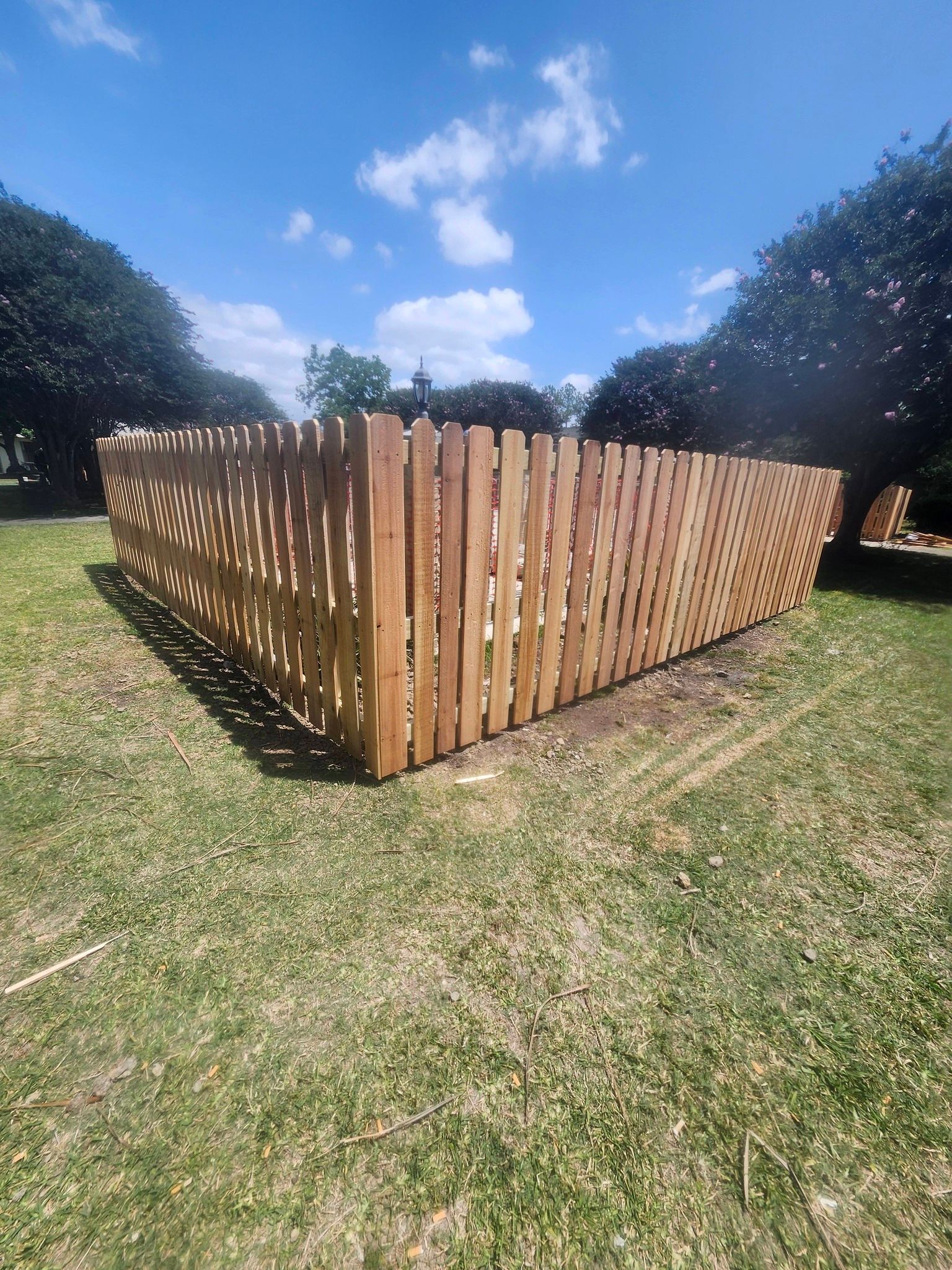 Wooden slat enclosure on a grassy lawn under a bright blue sky with trees in the background