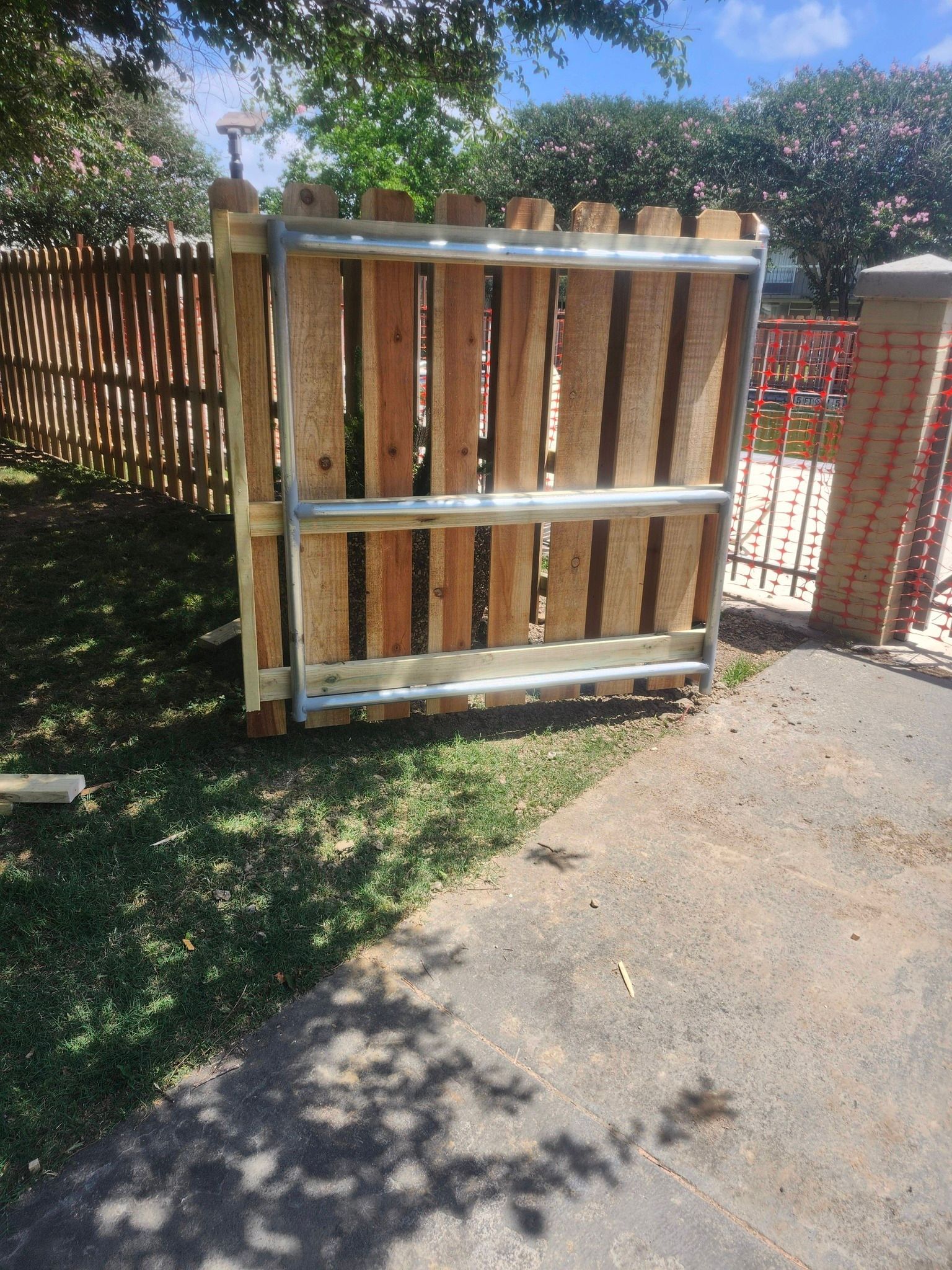 Wooden fence gate with metal frame beside a sidewalk in a sunny yard