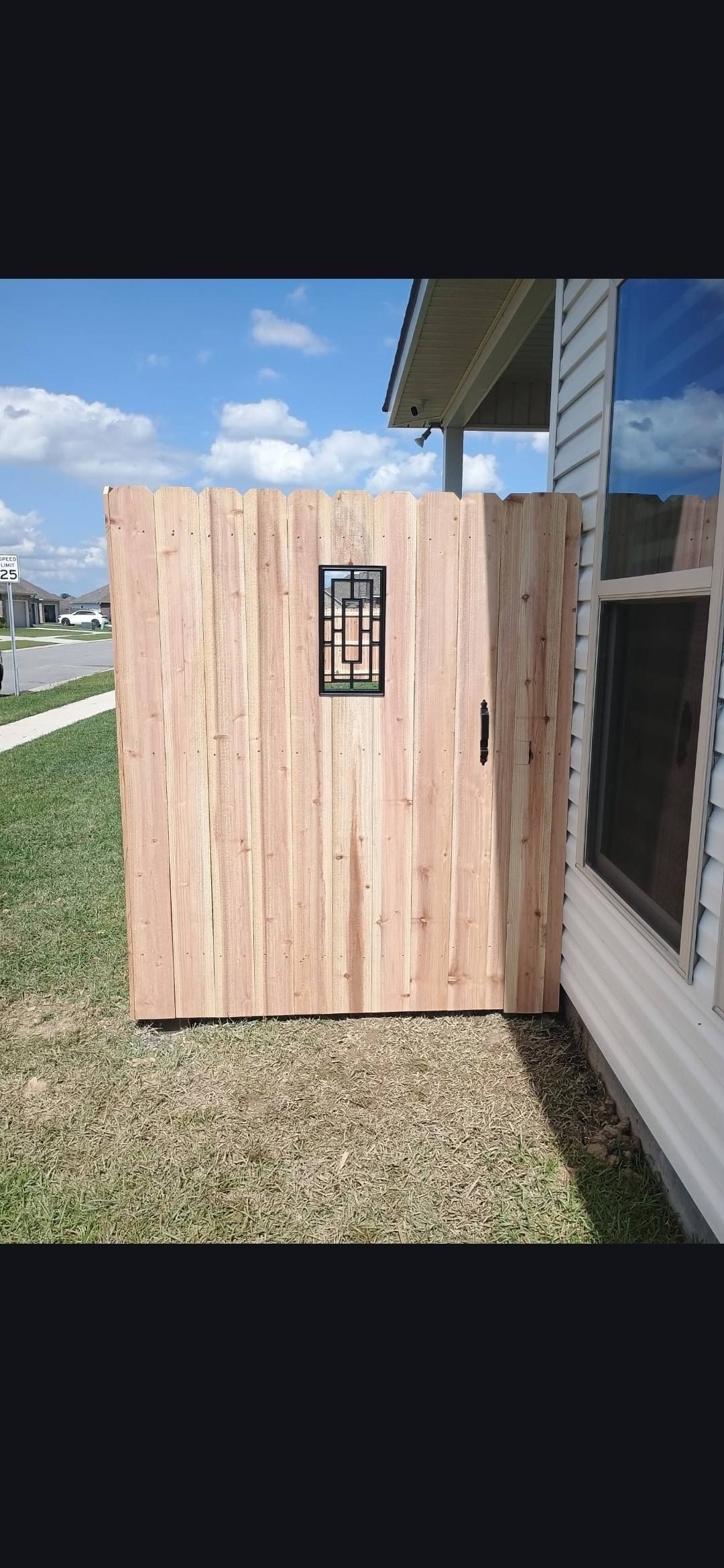 Wooden privacy screen beside a house with a small window opening on a sunny lawn.