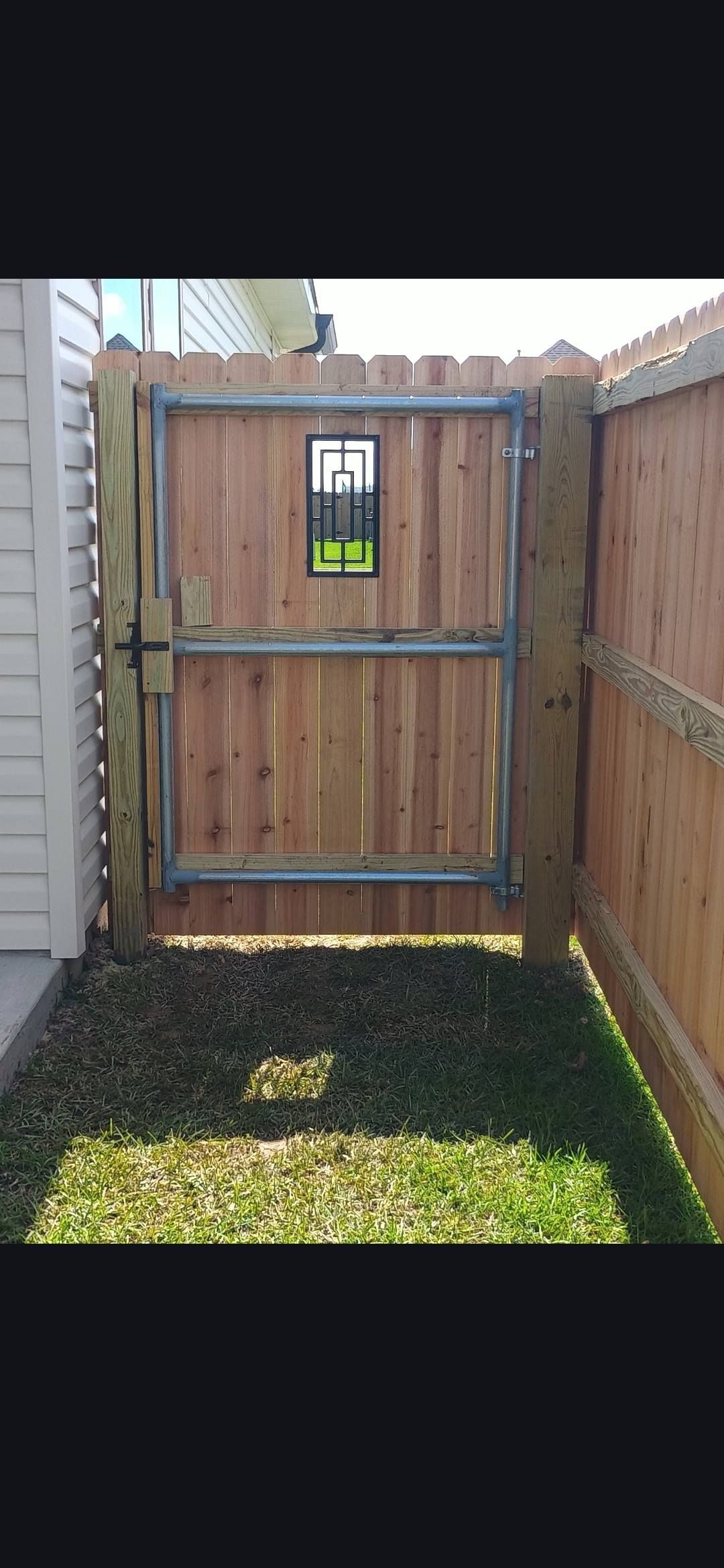 Wooden backyard fence gate with a small window, bordered by privacy fences and grass below.