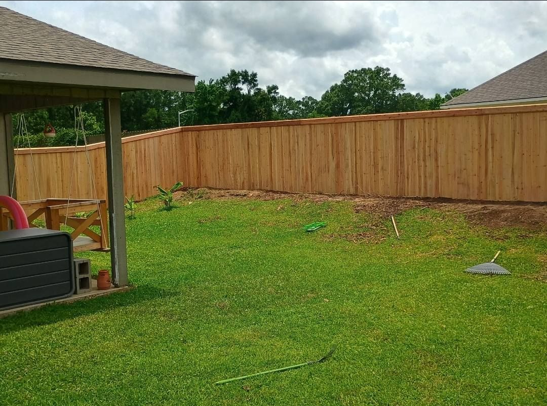 Backyard with a wooden fence, green lawn, cloudy sky, and a patio roof at left