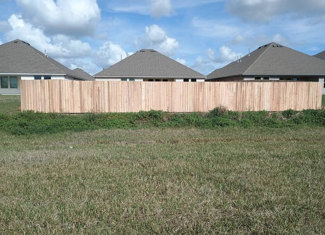 Wooden privacy fence in a grassy field with houses and cloudy sky behind it