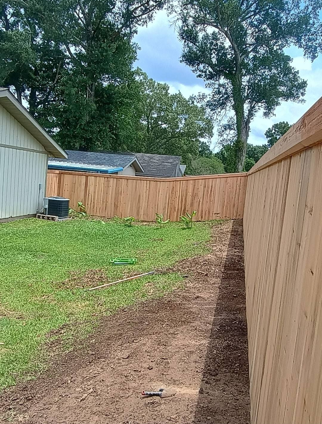 Backyard with a wooden privacy fence, green grass, and a bare dirt strip along the right side.
