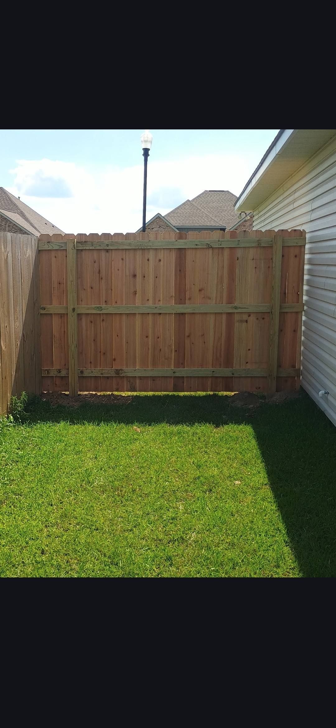 Wooden backyard fence between two houses, with green grass in front and a clear sky above