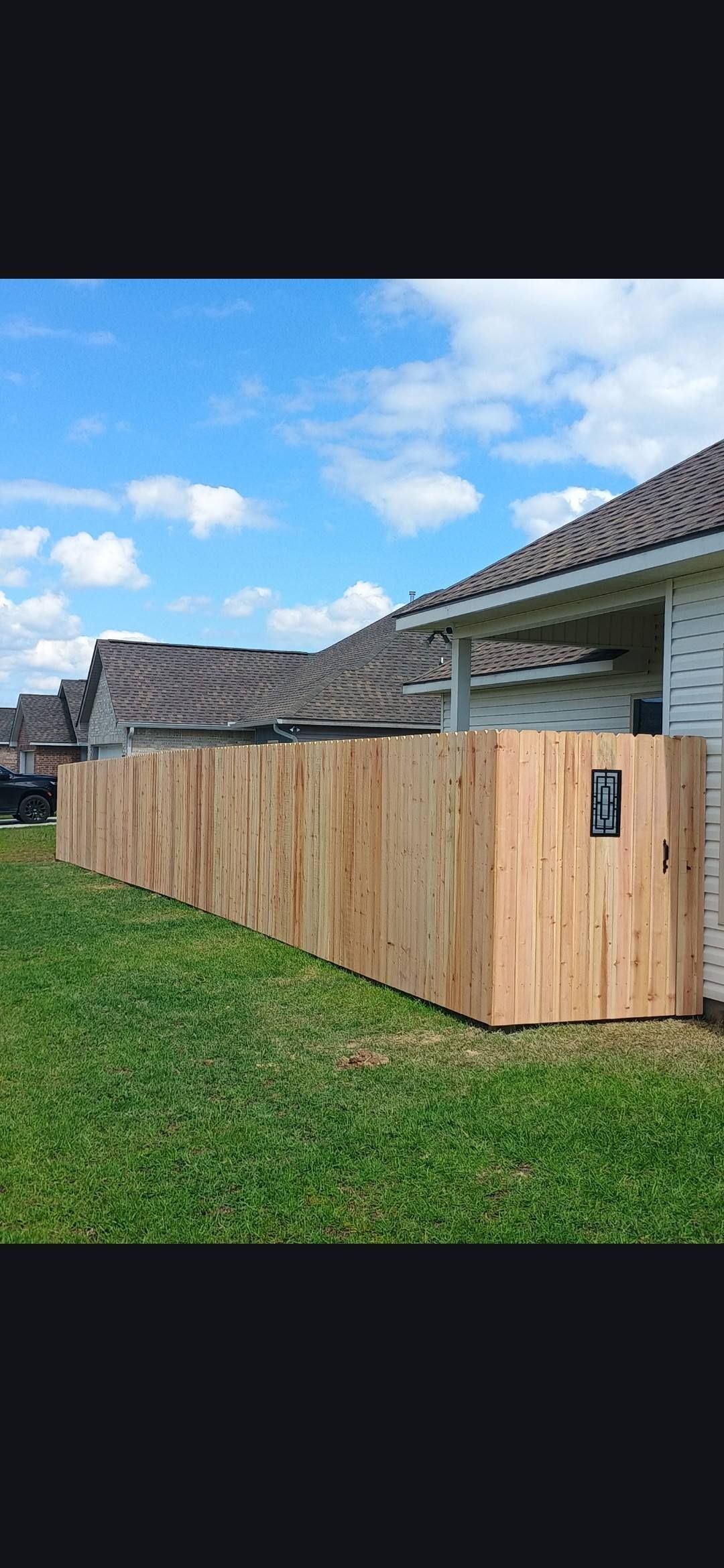 Wooden privacy fence along a grassy yard beside a house under a blue sky