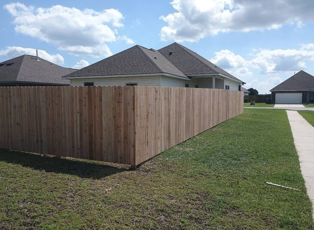 Suburban backyard with wooden privacy fence, green lawn, and neighboring houses under a cloudy sky