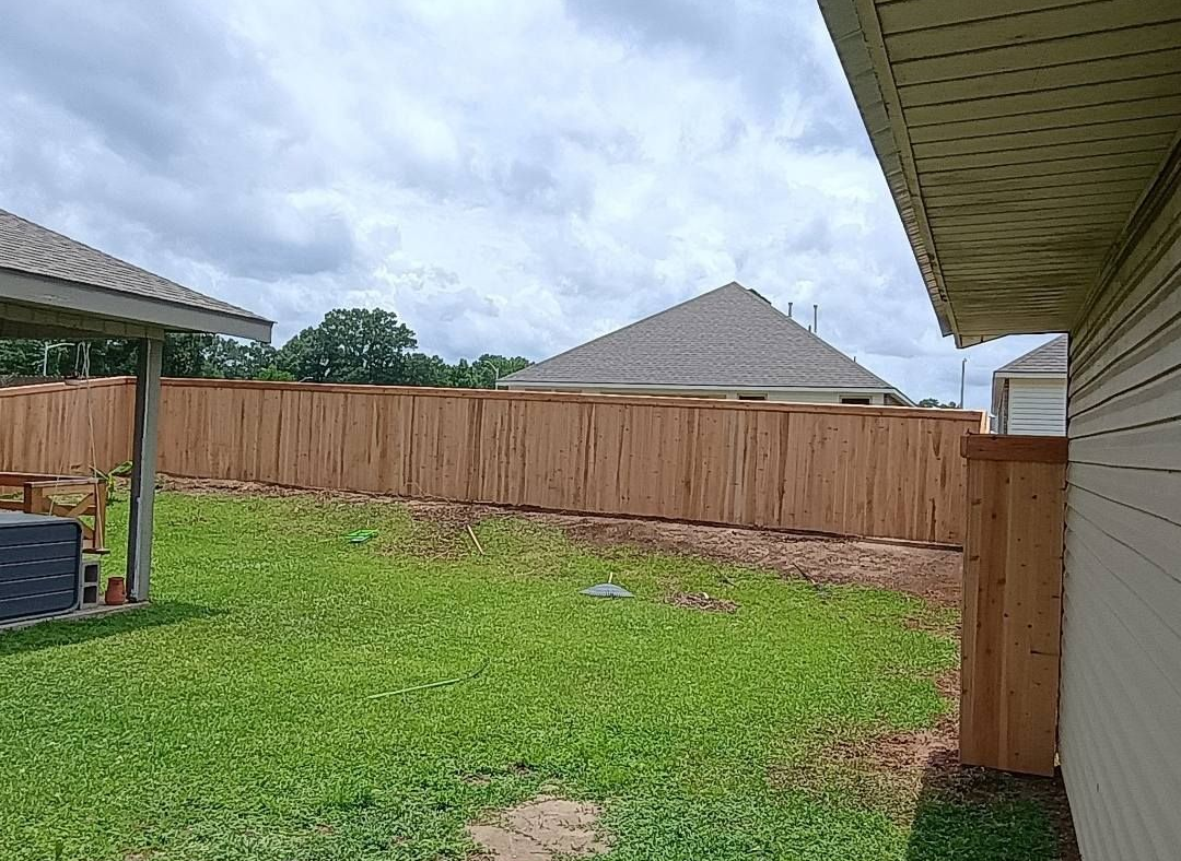 Backyard with green grass, wooden privacy fence, and cloudy sky beside a house