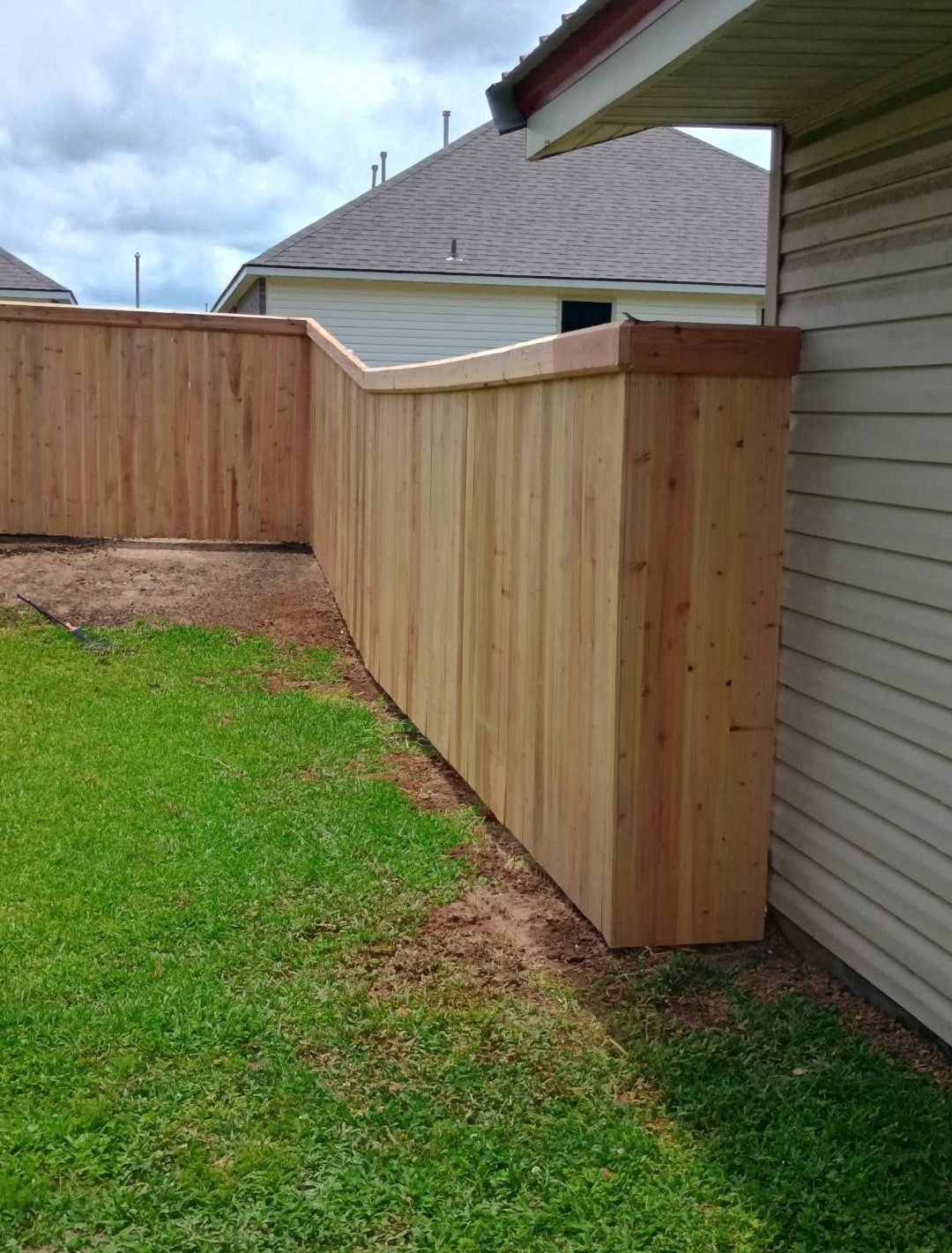 Wooden privacy fence along a house exterior beside a grassy yard.