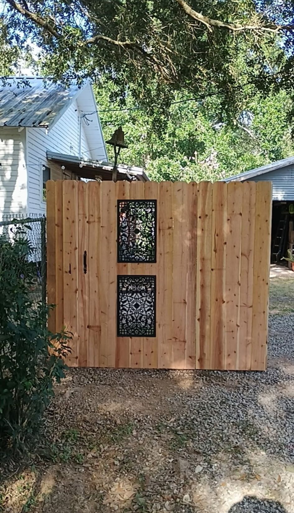 Wooden privacy fence with two decorative window panels in a tree-shaded backyard.