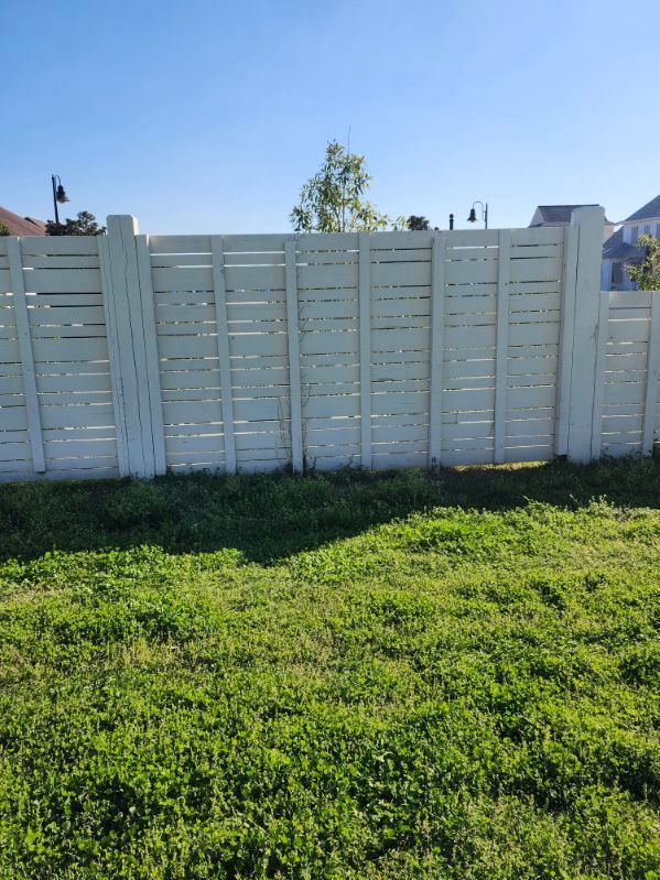 White fence behind a green grassy yard under a blue sky