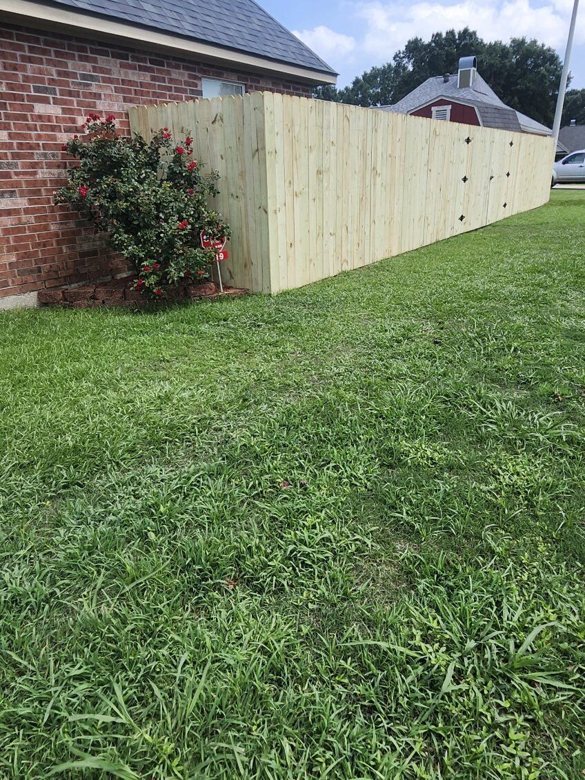 Fresh wooden fence beside a brick house, with a green lawn and shrub in the foreground
