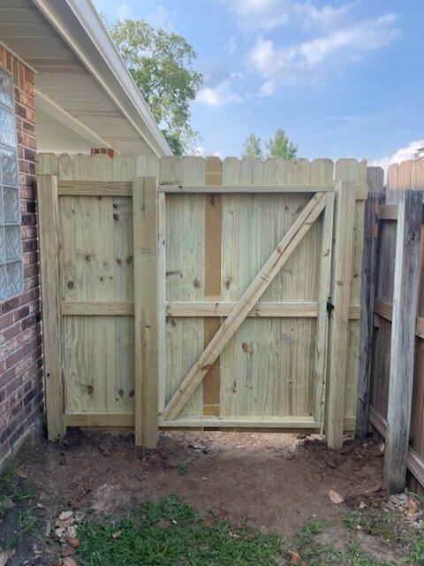 Wooden backyard gate with diagonal brace between fence sections beside a brick house.