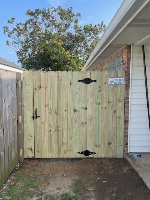 Wooden double gate in a fenced side yard beside a brick house and concrete driveway.