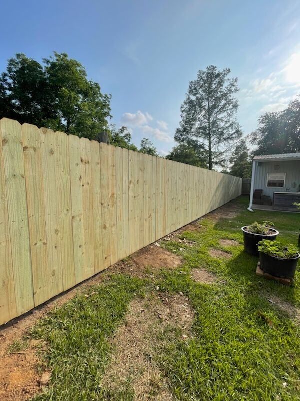 New wooden privacy fence along a grassy backyard beside a house and potted plants.
