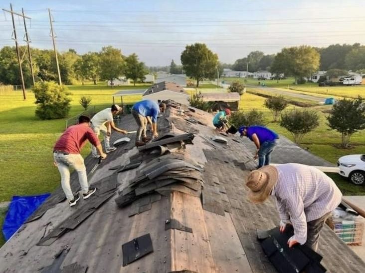 Workers repairing a damaged roof on a house, with dark shingles spread across the roofline.