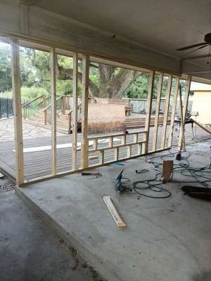Unfinished room with exposed wall framing, concrete floor, tools, and a view of a deck outside.