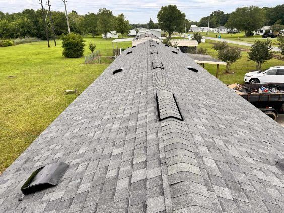 Roof shingles with several lifted vents on a long house roof in a green suburban area