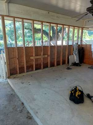 Empty garage with exposed wooden framing, concrete floor, and a tool bag on the ground.