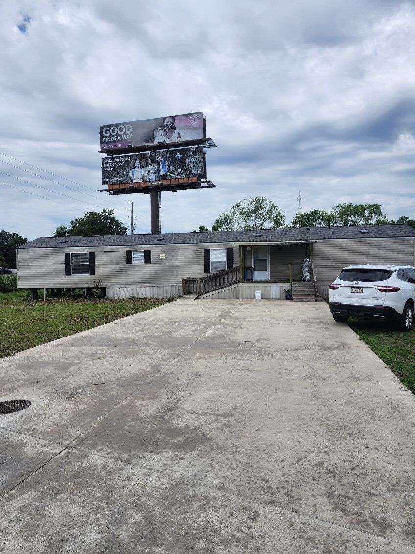 Single-story building with a large billboard, long driveway, and a white SUV under a cloudy sky