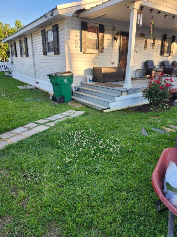 White house with a front porch, green lawn, and a trash bin near the steps.