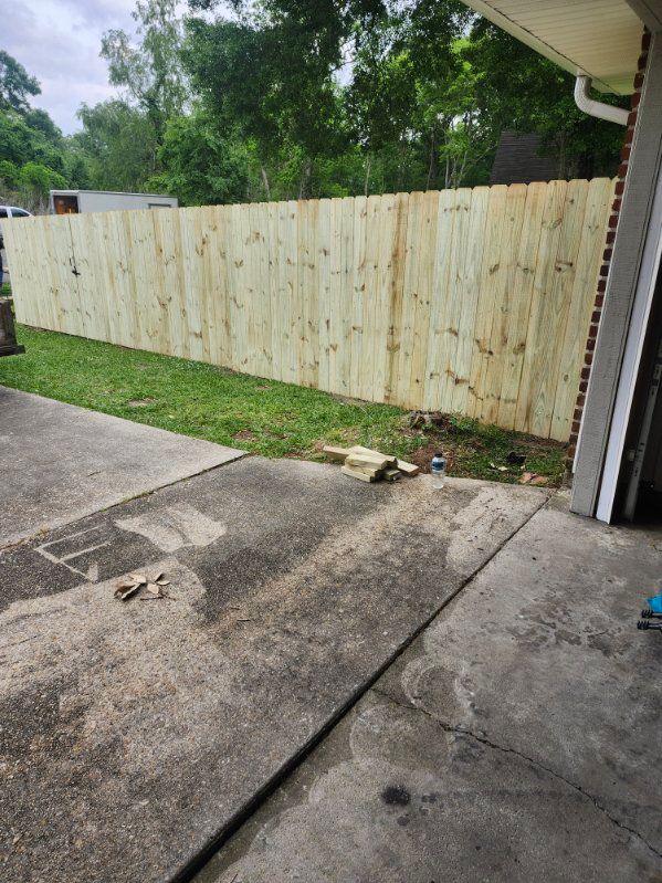 Concrete driveway beside a green lawn and weathered wooden fence, with a garage edge on the right.