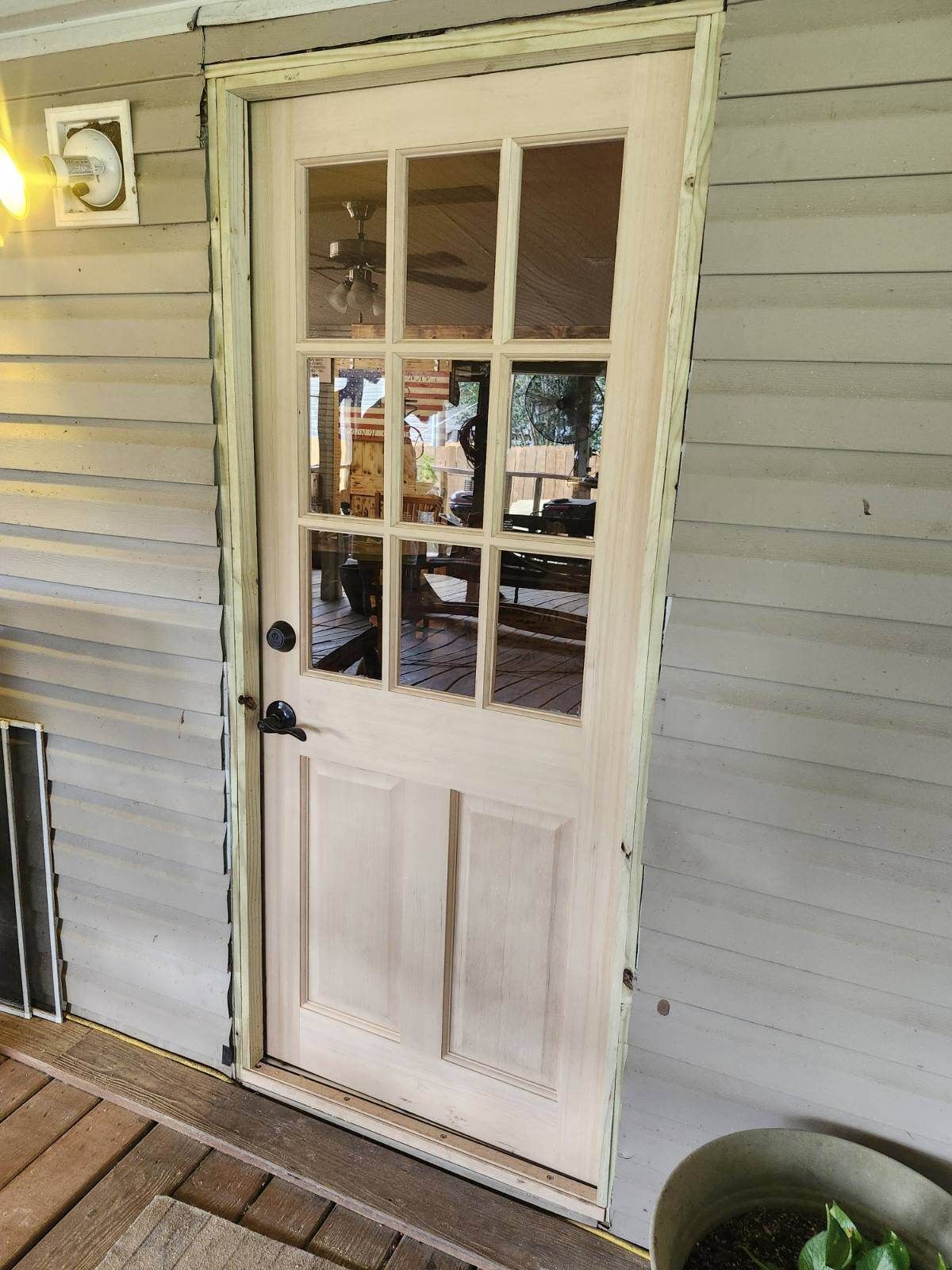 White paneled exterior door with glass panes on a house porch, beside beige siding and a wall light.