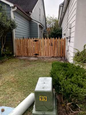 Narrow backyard between houses with a wooden fence and utility box in the foreground