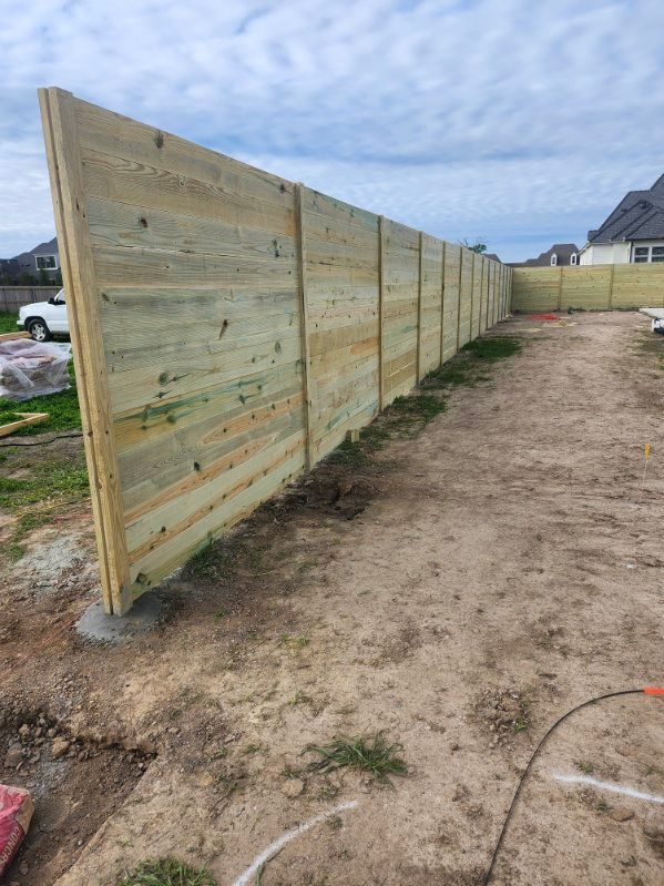 Long wooden fence panels along a dirt yard under a cloudy sky