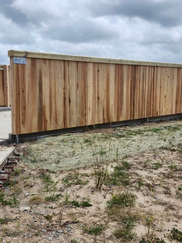 Wooden shed with vertical planks on a grassy, muddy lot under cloudy skies.
