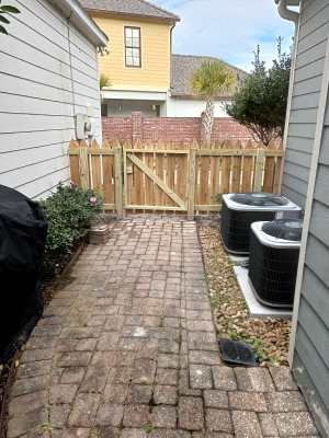 Brick patio path leading to a wooden gate between houses, with outdoor HVAC units on the right.