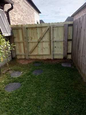 Small backyard with grass, stepping stones, and a wooden gate between brick and wood fences
