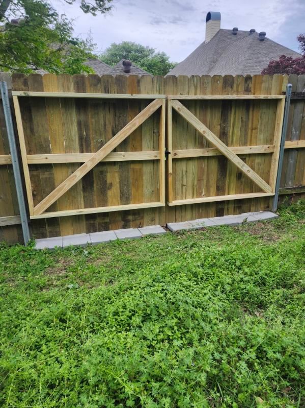 Wooden backyard fence gate with diagonal braces and gray cinder blocks at the base, in front of grass.