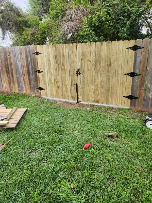 Wooden fence in a grassy backyard with trees behind it and a red toy on the lawn.