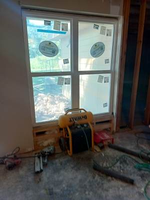 Partially installed window in a room under renovation, with tools and construction materials on the floor